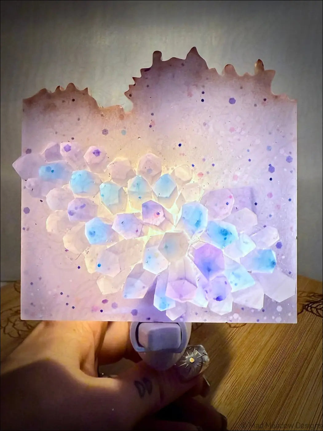 A glowing crystal cluster wall night light with translucent blue and purple faceted crystals on a lavender background