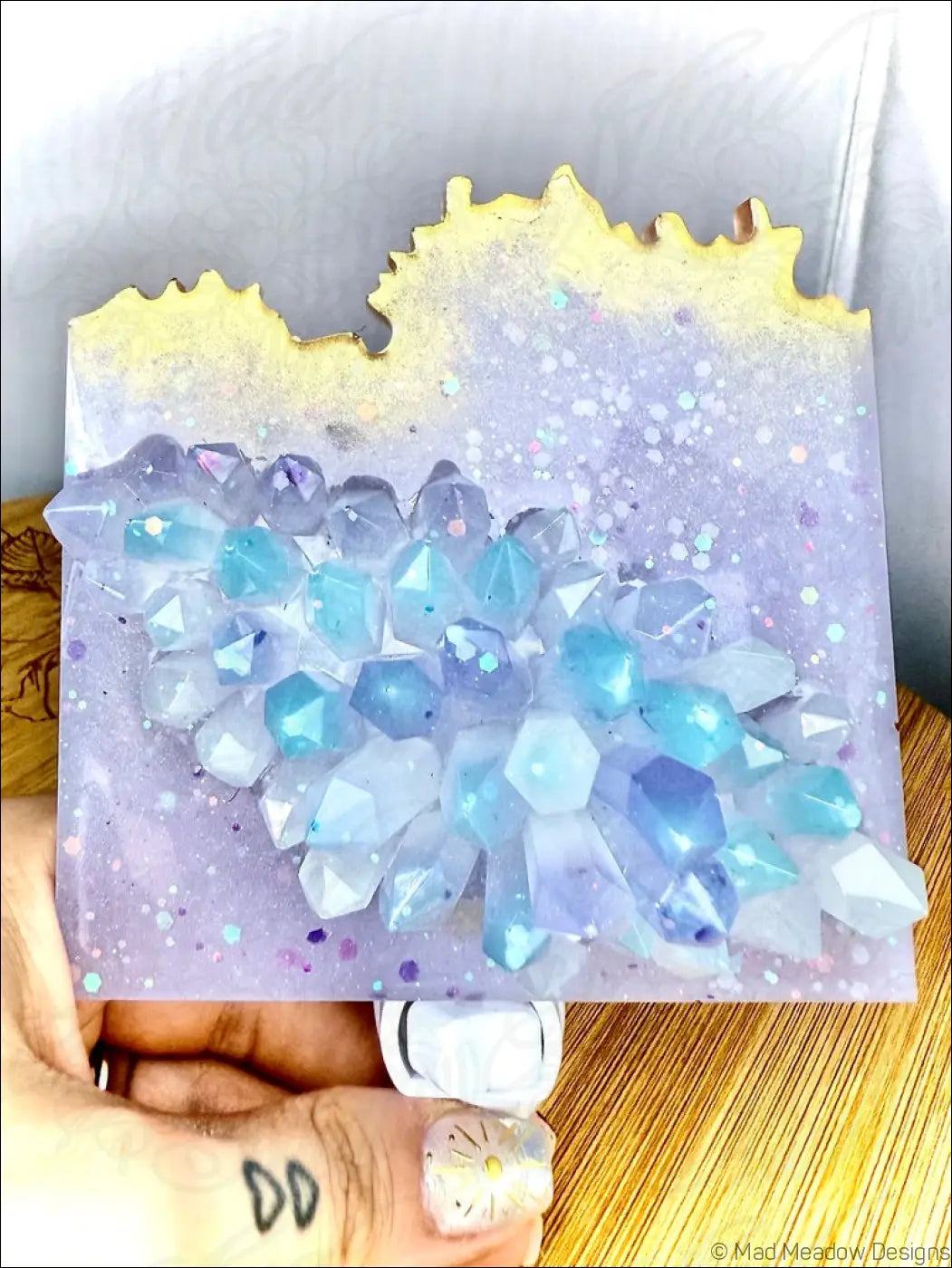 A hand holds a glowing crystal cluster wall night light with blue and purple resin crystals on a plug-in base