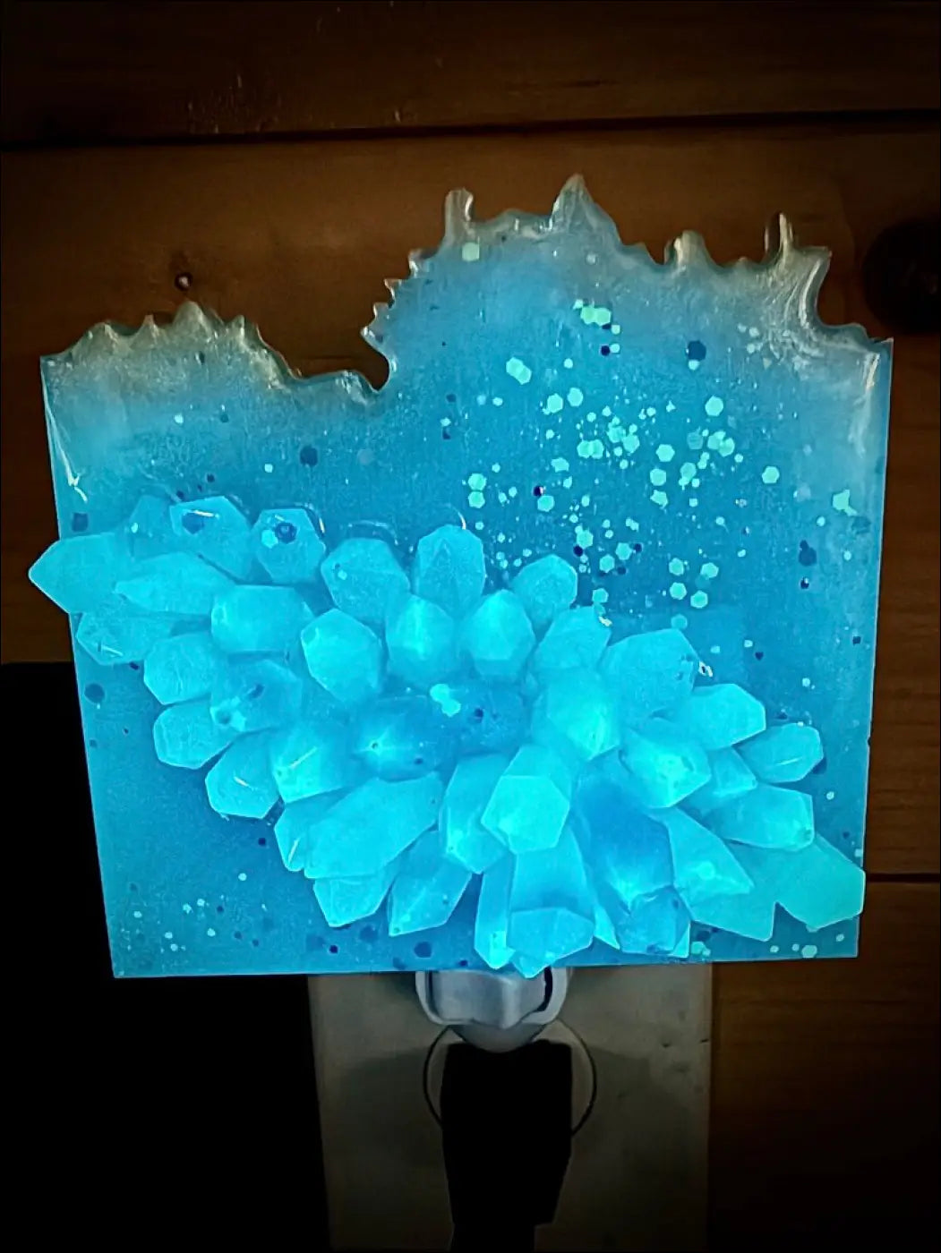 A glowing crystal cluster night light in blue and purple resin with embedded crystals on a plug-in wall base