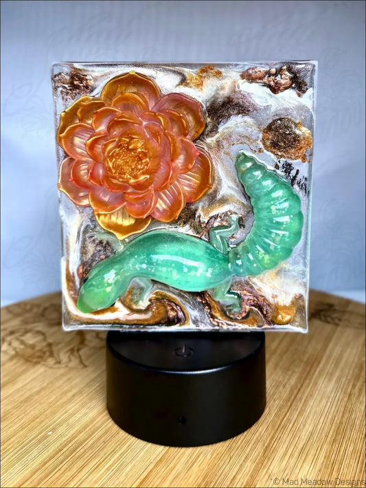 A square resin pink lotus nightlight with an enchanting glowing gecko and shimmering gold accents in amber swirls