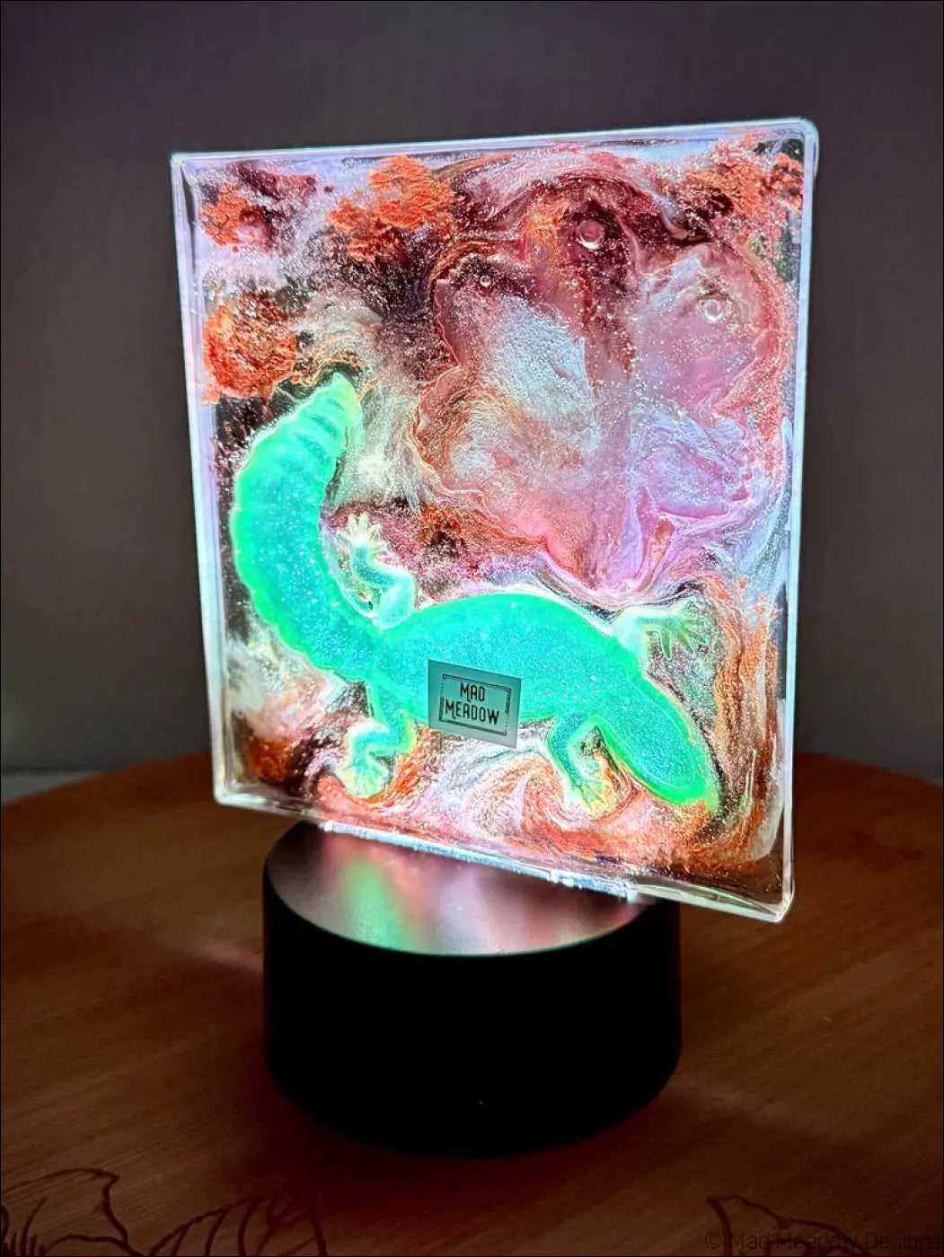 A glowing turquoise dinosaur resin art on a black base with shimmering gold accents perfect as a pink lotus nightlight