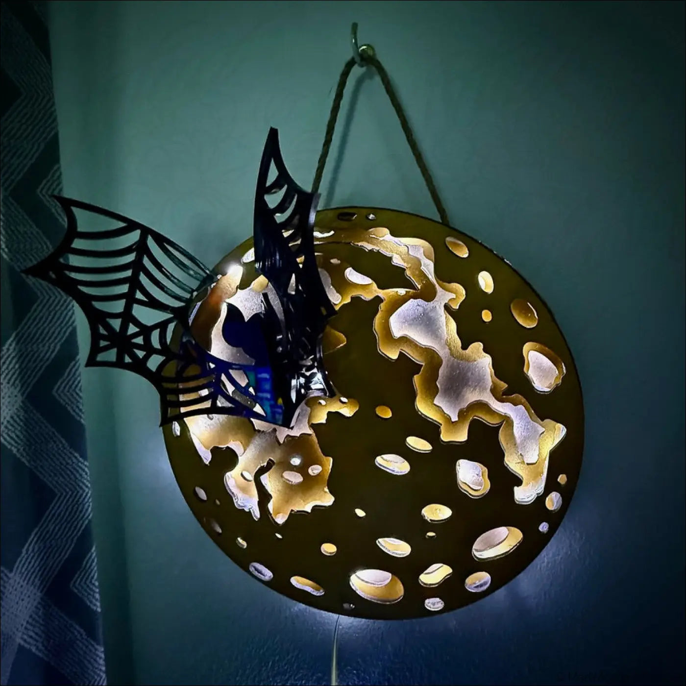 Black metal spiderweb and bat decoration hanging from a gold glowing moon light with enchanting laser-cut wood details
