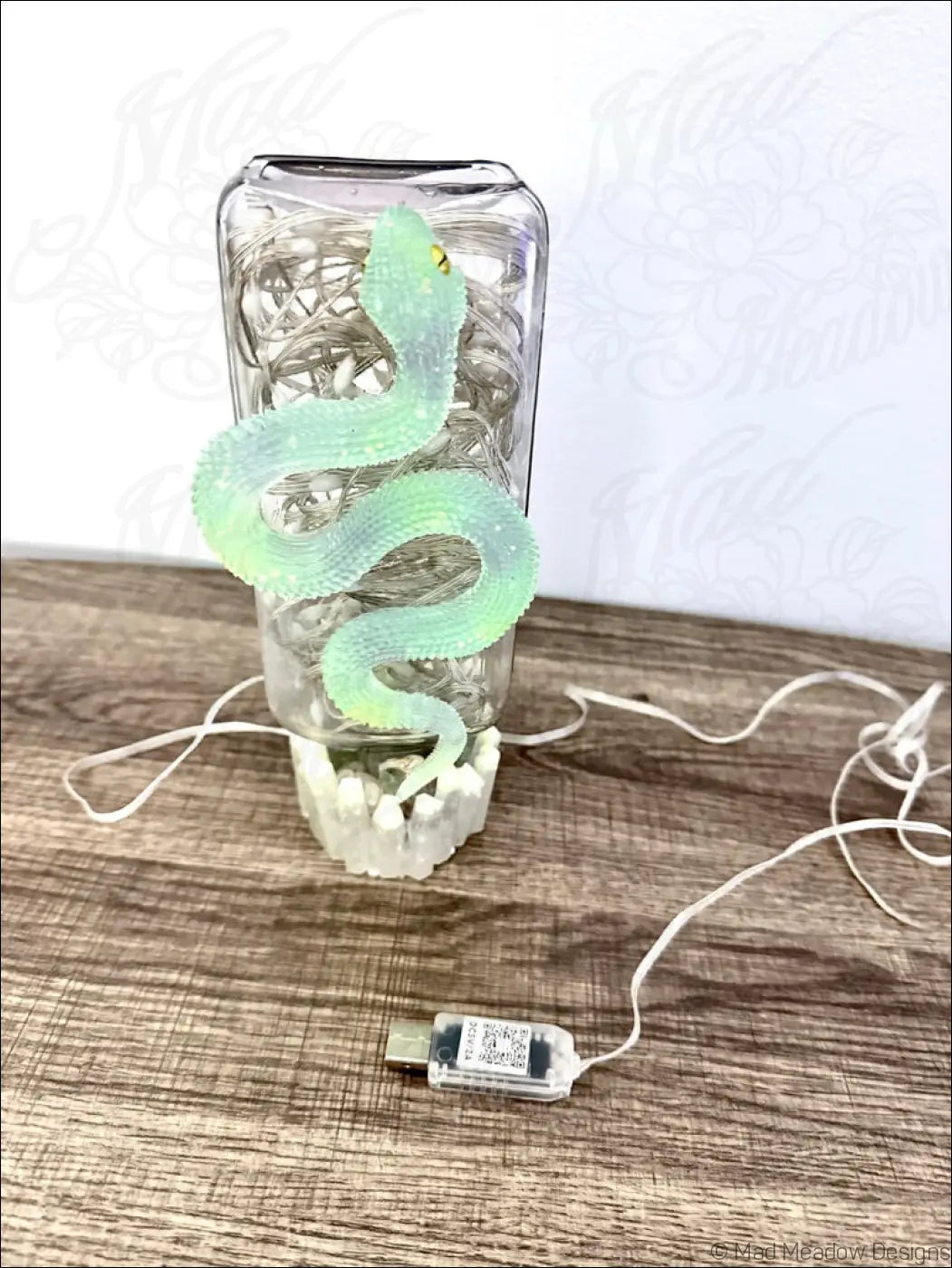 A translucent green snake-shaped decorative usb lamp coiled around a clear glass apothecary jar with string lights