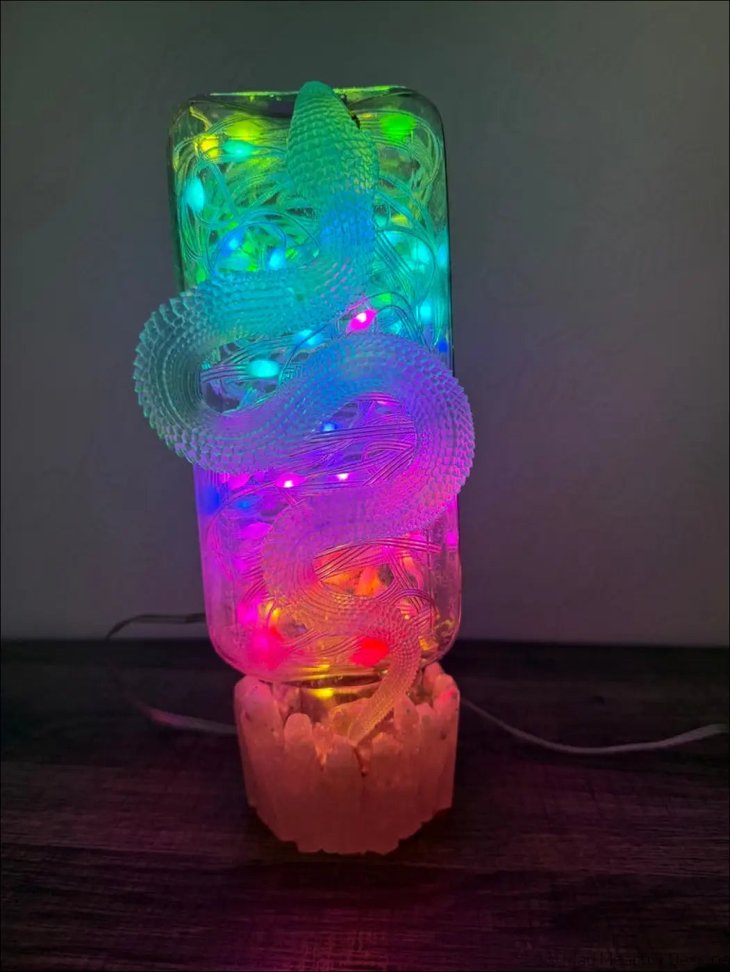 A translucent multi-colored led lamp with an intricately carved dragon inside a rectangular glass apothecary bottle