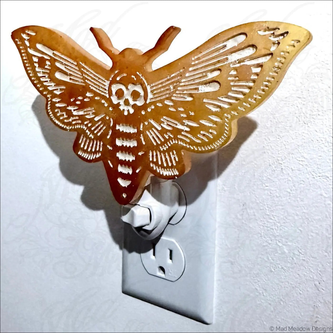Translucent amber gold death moth resin wall night light with skull design plugged into electrical outlet