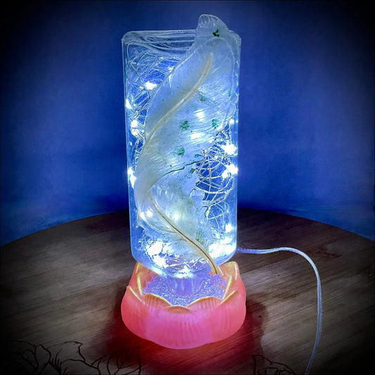 A translucent antique glass apothecary bottle with glowing white feather and fairy lights on red-orange lotus usb base