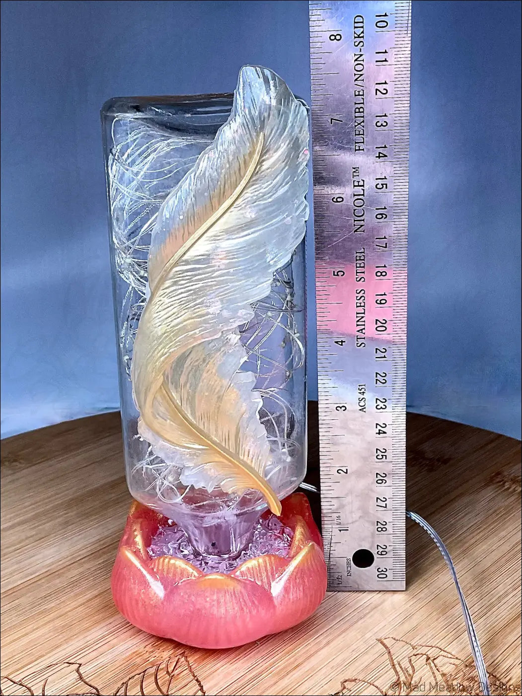 A translucent golden feather sculpture inside an antique glass apothecary bottle on a red-orange lotus base usb light