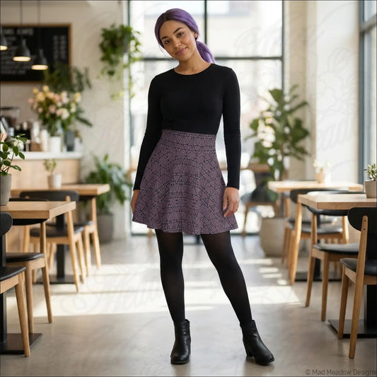A flared purple grape elemental column pattern skater skirt worn over black leggings with a black top care instructions line dry
