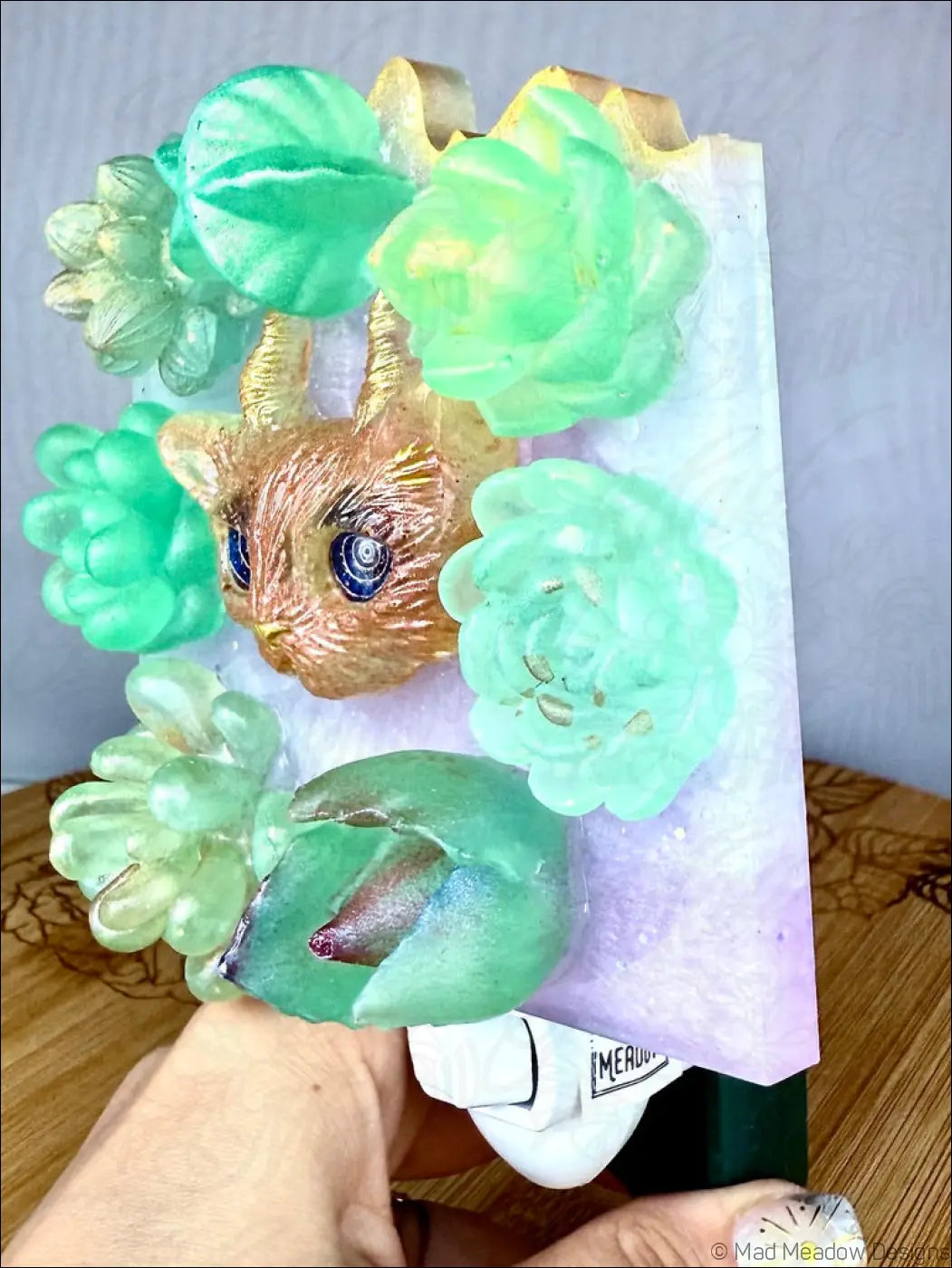 A whimsical horned kitty cat soap bar with blue eyes and green succulent accents for garden wall night light use