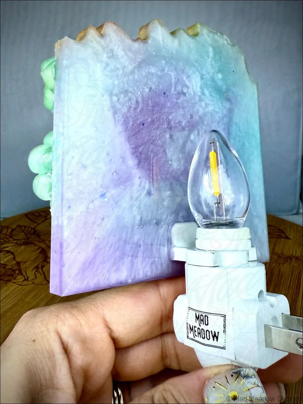 A hand holds a horned kitty cat garden wall night light with a clear bulb and colorful purple blue resin panel