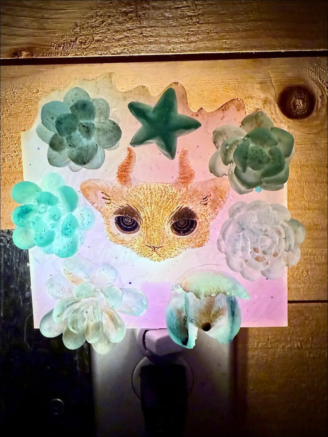 A horned kitty cat garden wall night light with a glittery orange cat face and green blue succulent details on plug-in base