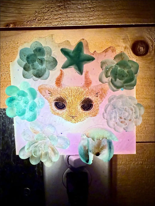 A horned kitty cat garden wall night light with a glittery orange cat face and green blue succulent details on plug-in base