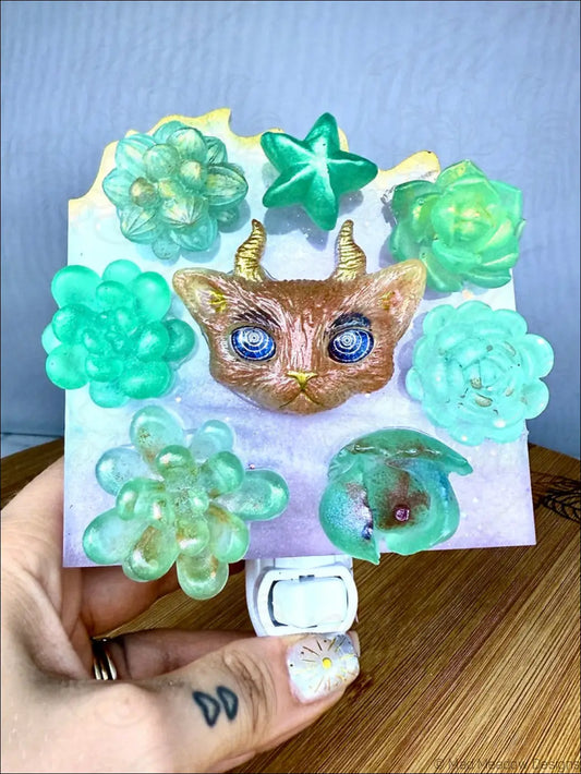 A whimsical brown resin horned kitty cat with glowing blue eyes on a garden wall night light plug-in base