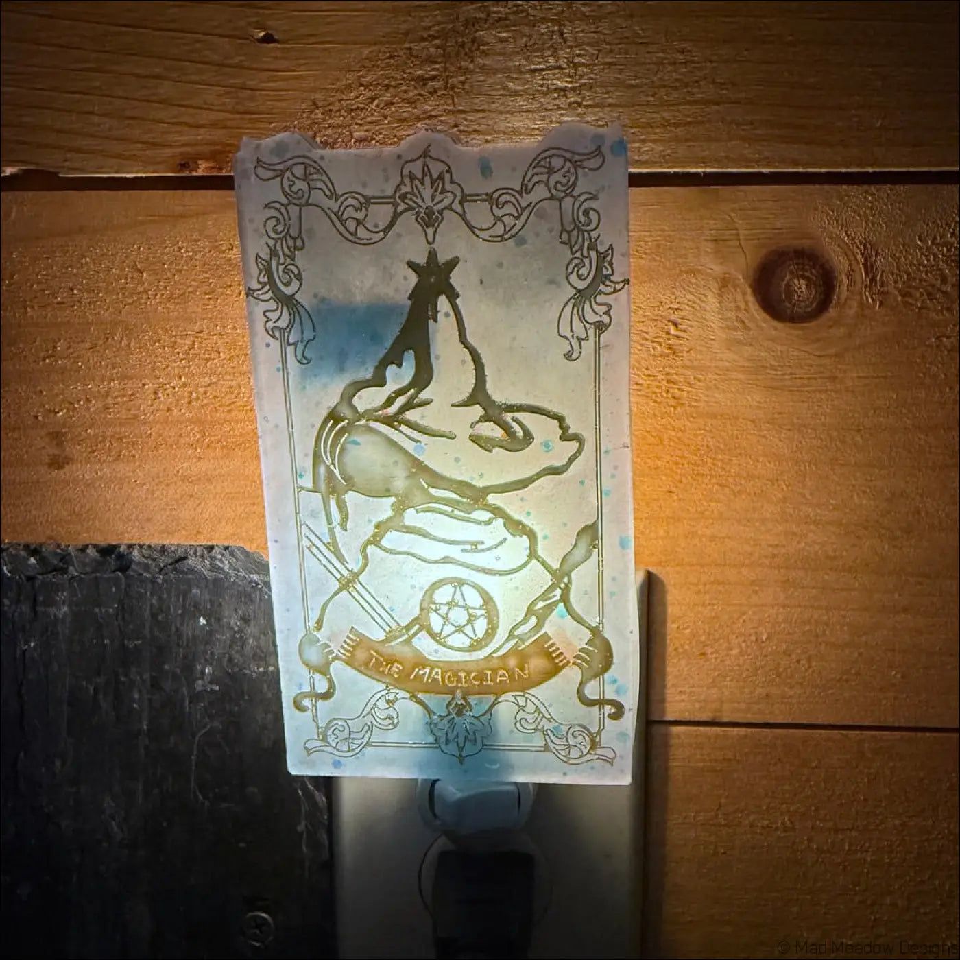 A translucent frosted glass tarot resin wall night light with a mesmerizing magician tarot gold-etched design on plug-in base