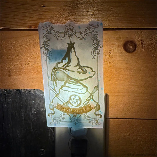 A translucent frosted glass tarot resin wall night light with a mesmerizing magician tarot gold-etched design on plug-in base