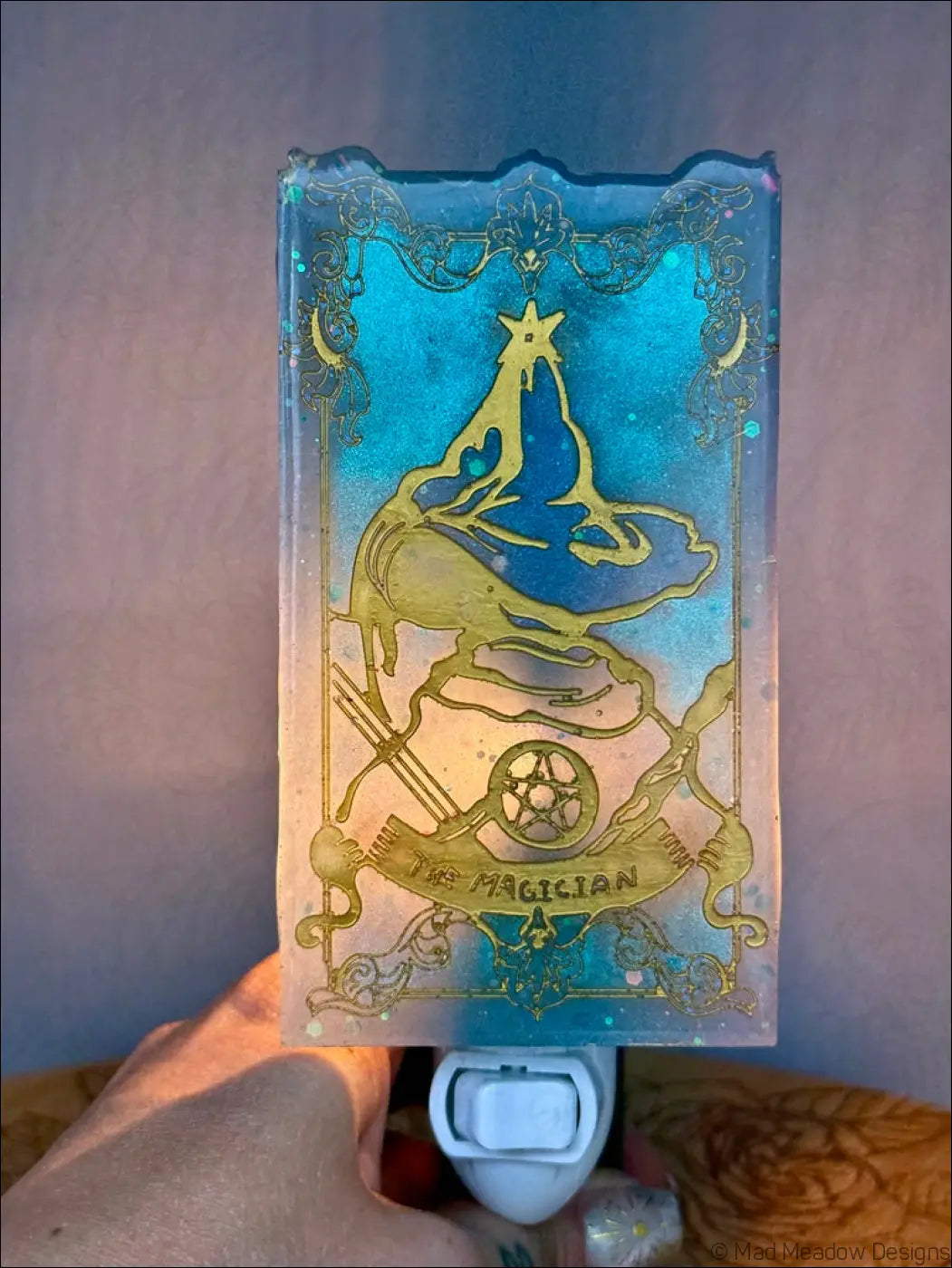 Translucent blue and gold resin nightlight with mesmerizing magician tarot design on a plug-in tarot resin wall lamp