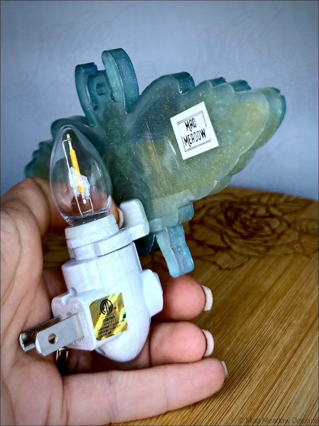 A translucent teal iridescent scarab resin wall night light with clear bulb and white plug base showing aqua blue hues