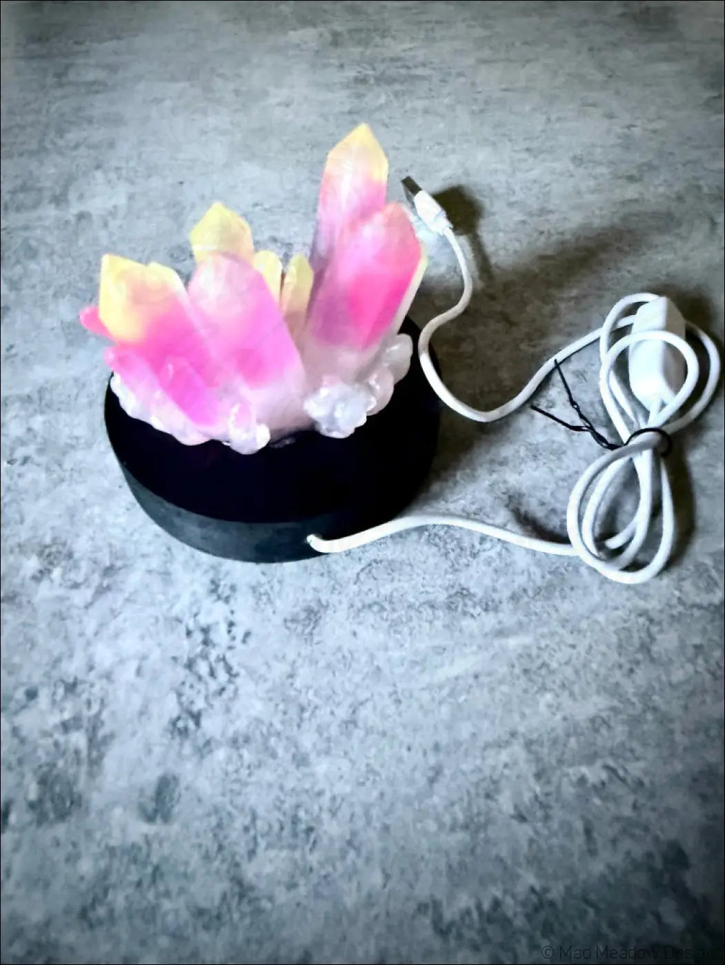 Large resin crystal cluster lamp with pink and yellow resin crystals glowing on a wooden black base