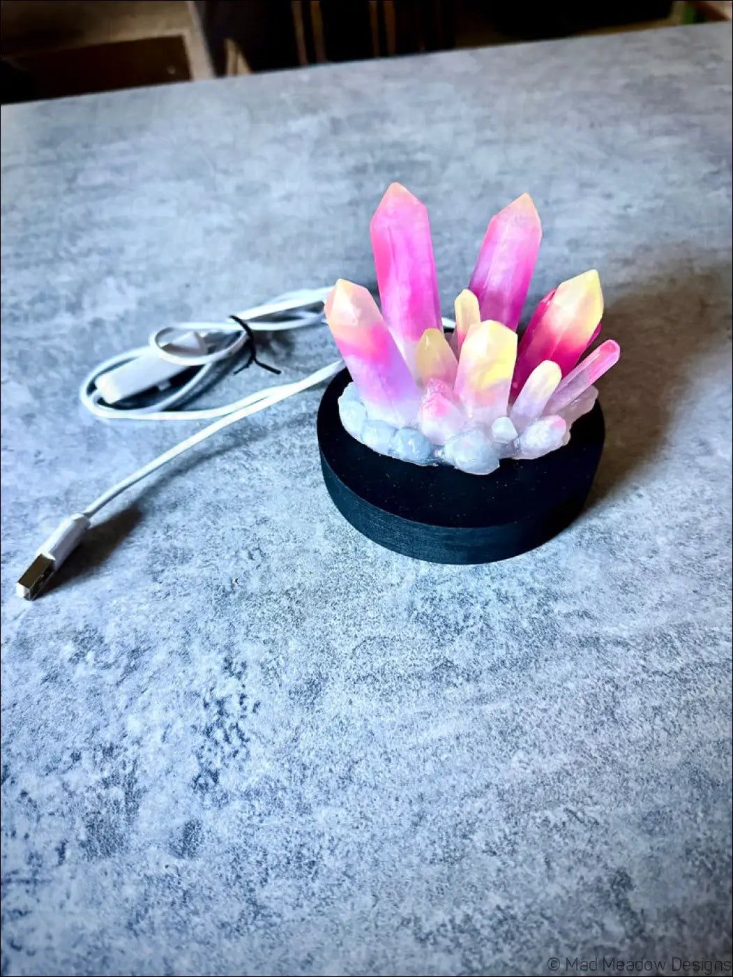 A vibrant pink and yellow resin crystal cluster glow in the dark centerpiece on a black wooden base