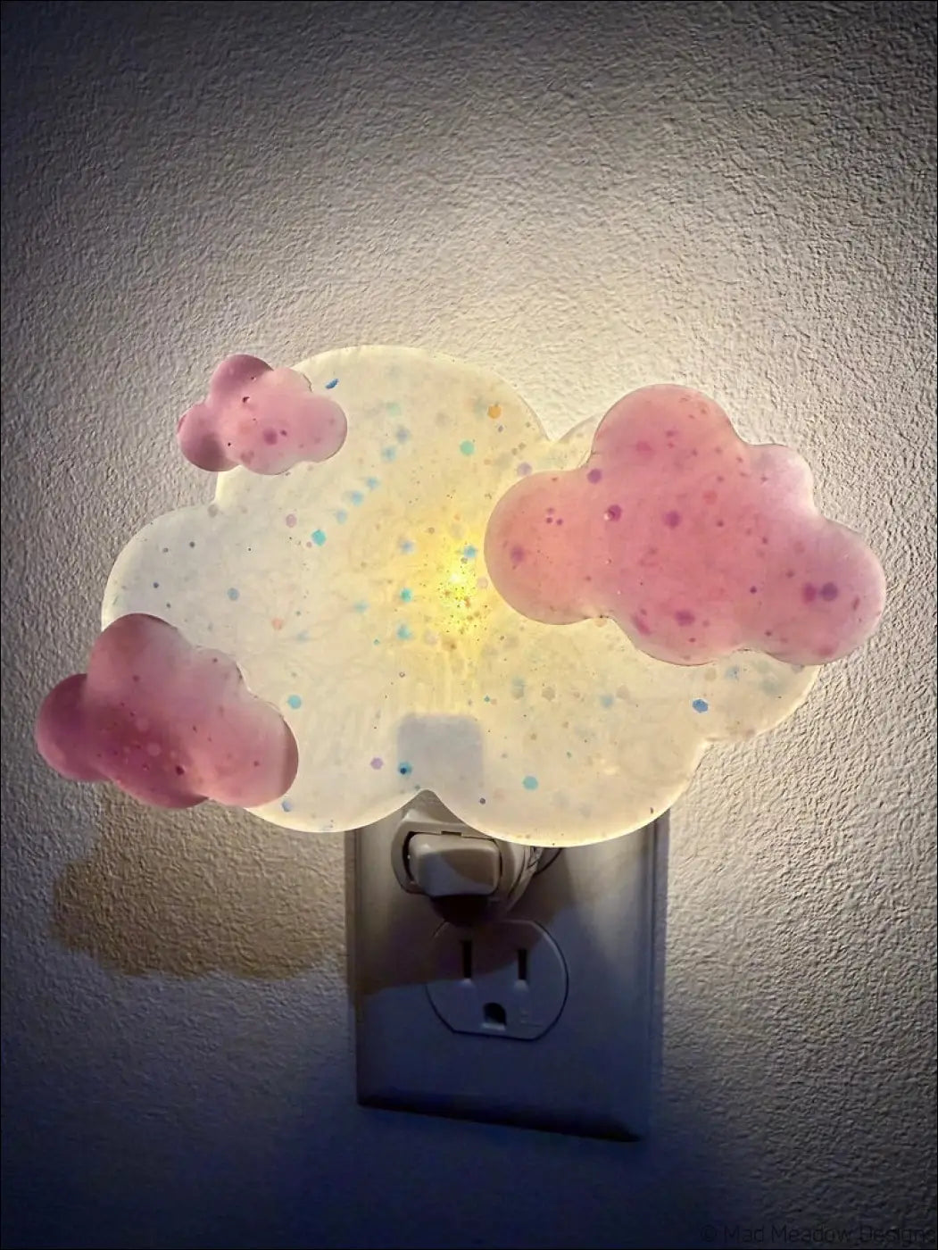 Magenta clouds wall night light by mad meadow designs with glowing pink cloud shape and colorful glitter speckles on plug-in base