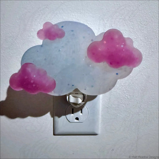 Magenta clouds wall night light by mad meadow designs featuring a translucent white base and pink glittery cloud shapes