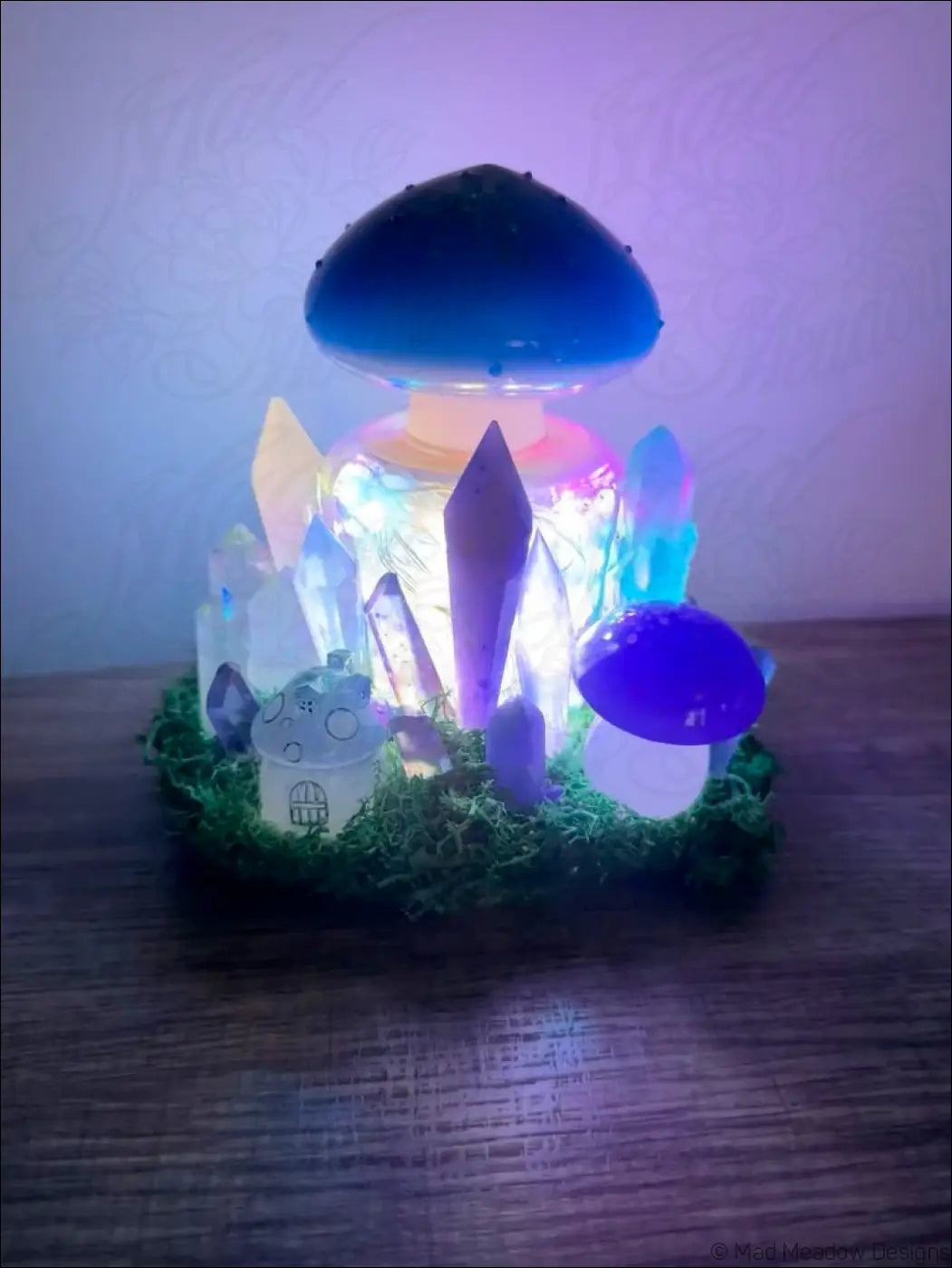 A glowing blue usb light shaped like a mushroom with crystal accents and a miniature house in green moss