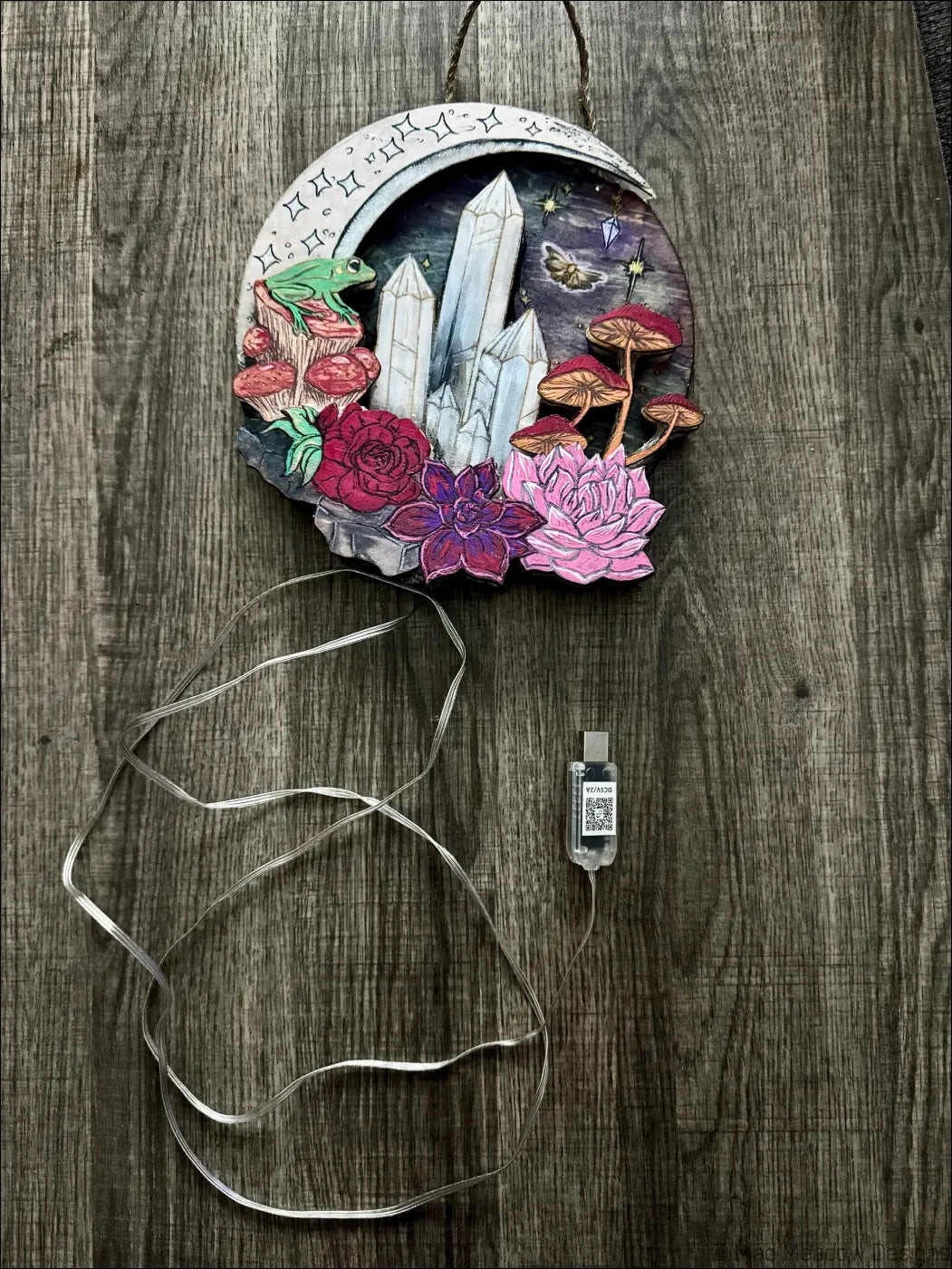 A whimsical crescent moon wooden USB light with hand-painted crystals mushrooms and frog in a mushroom forest ablaze style