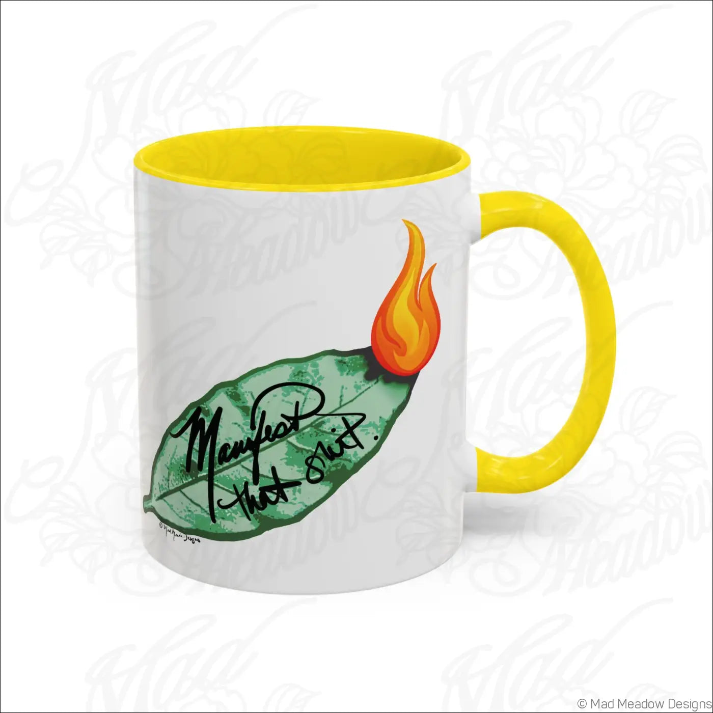 White ceramic coffee mug with glossy finish, yellow colored interior and handle, green bay leaf and orange flame design with manifest that shit text