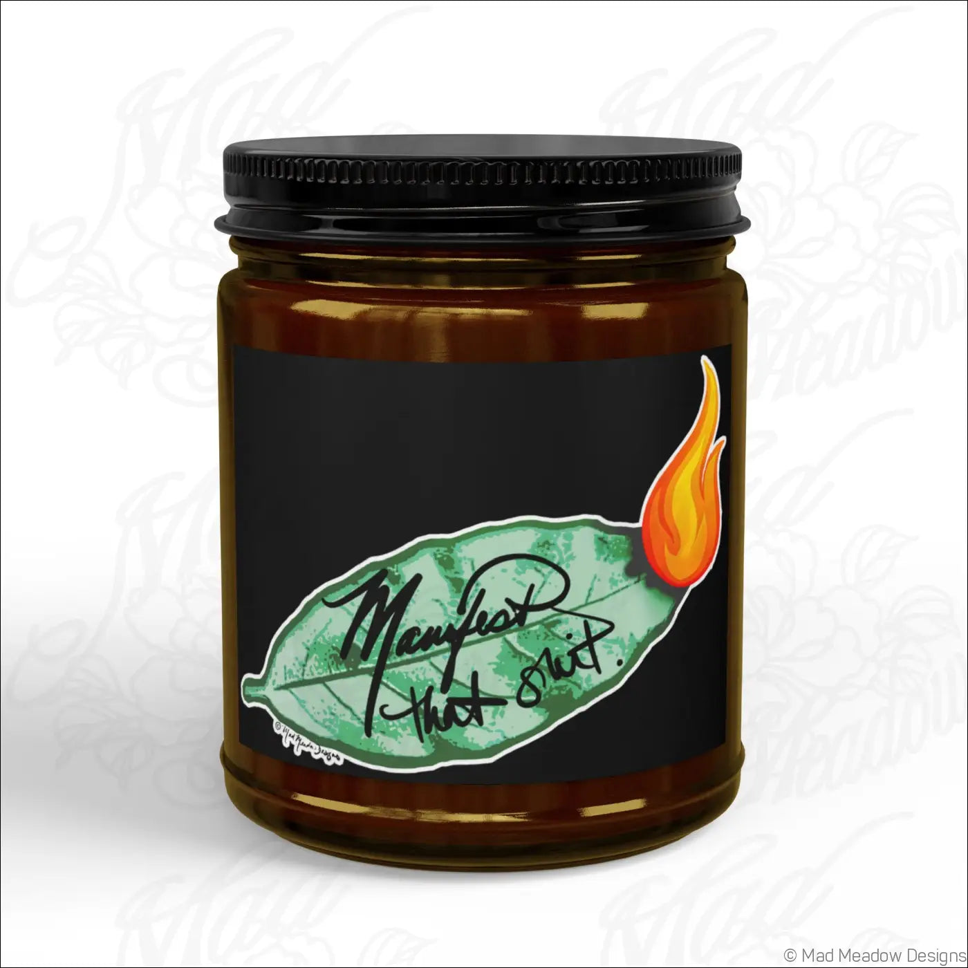 Brown glass jar soy wax candle with black lid and manifest that shit label featuring green leaf and orange flame design