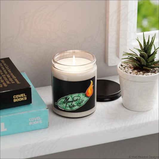 A white soy candle in a clear glass jar with a bay leaf design and orange flame from manifest that sh*t soy wax blend