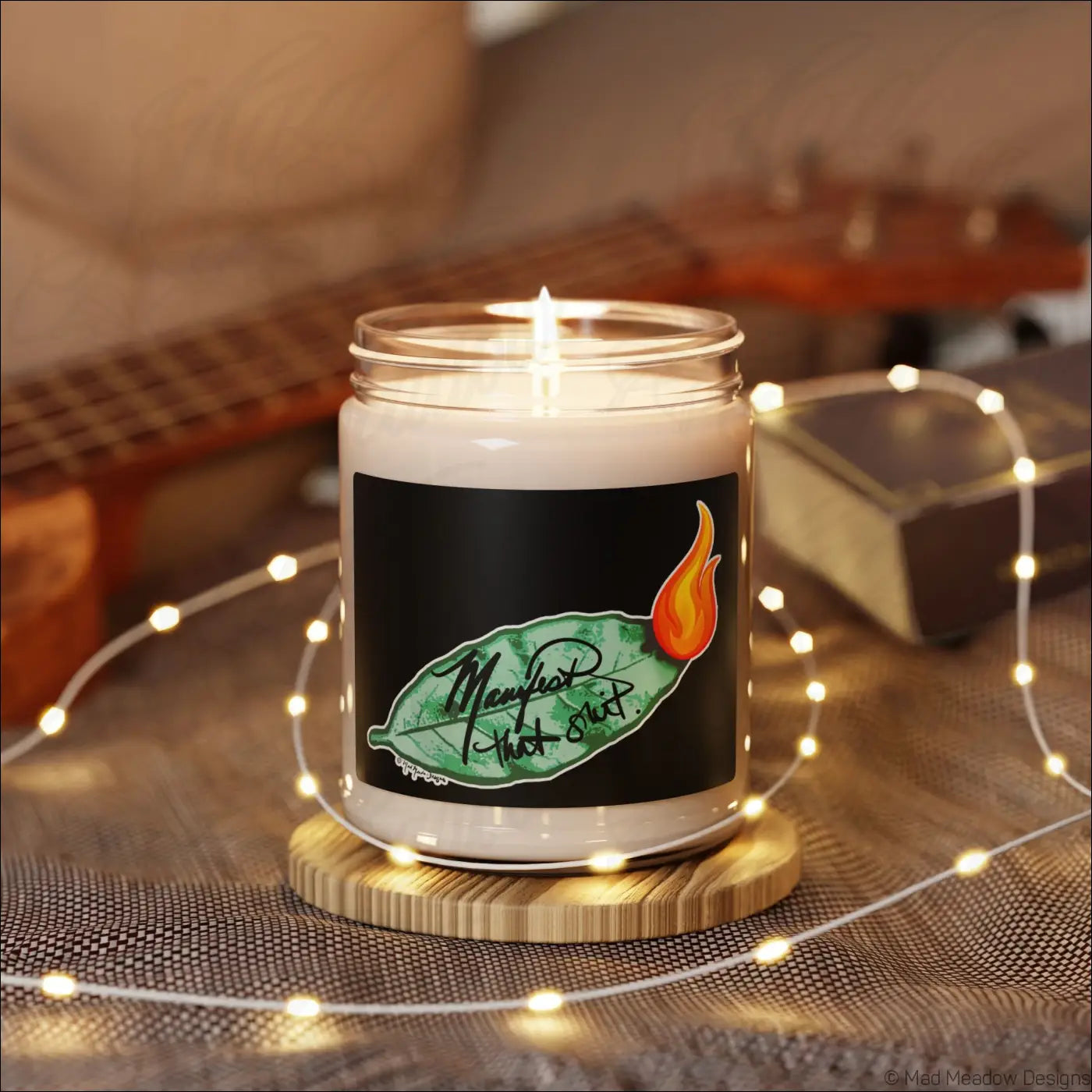A white soy candle in a clear glass jar with a black label showing a green bay leaf and orange flame design