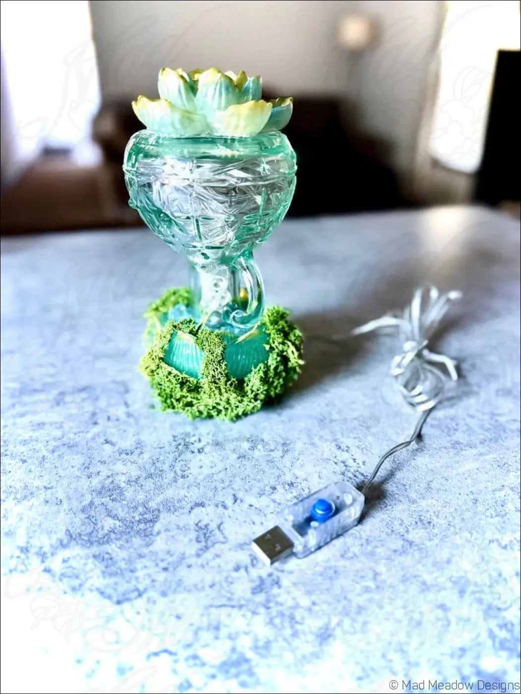 Mint green lotus flower lamp made of translucent vintage glass with moss base and usb power adapter nearby