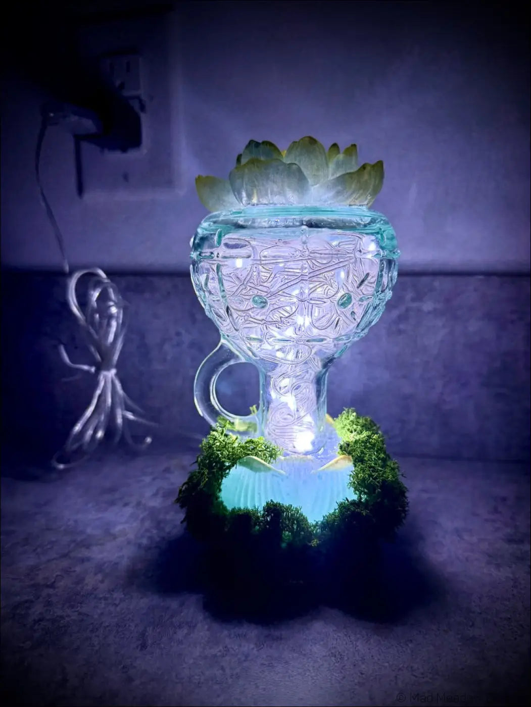 A vintage glass usb lamp glowing softly with intricate etched patterns topped with a mint green and gold lotus plant