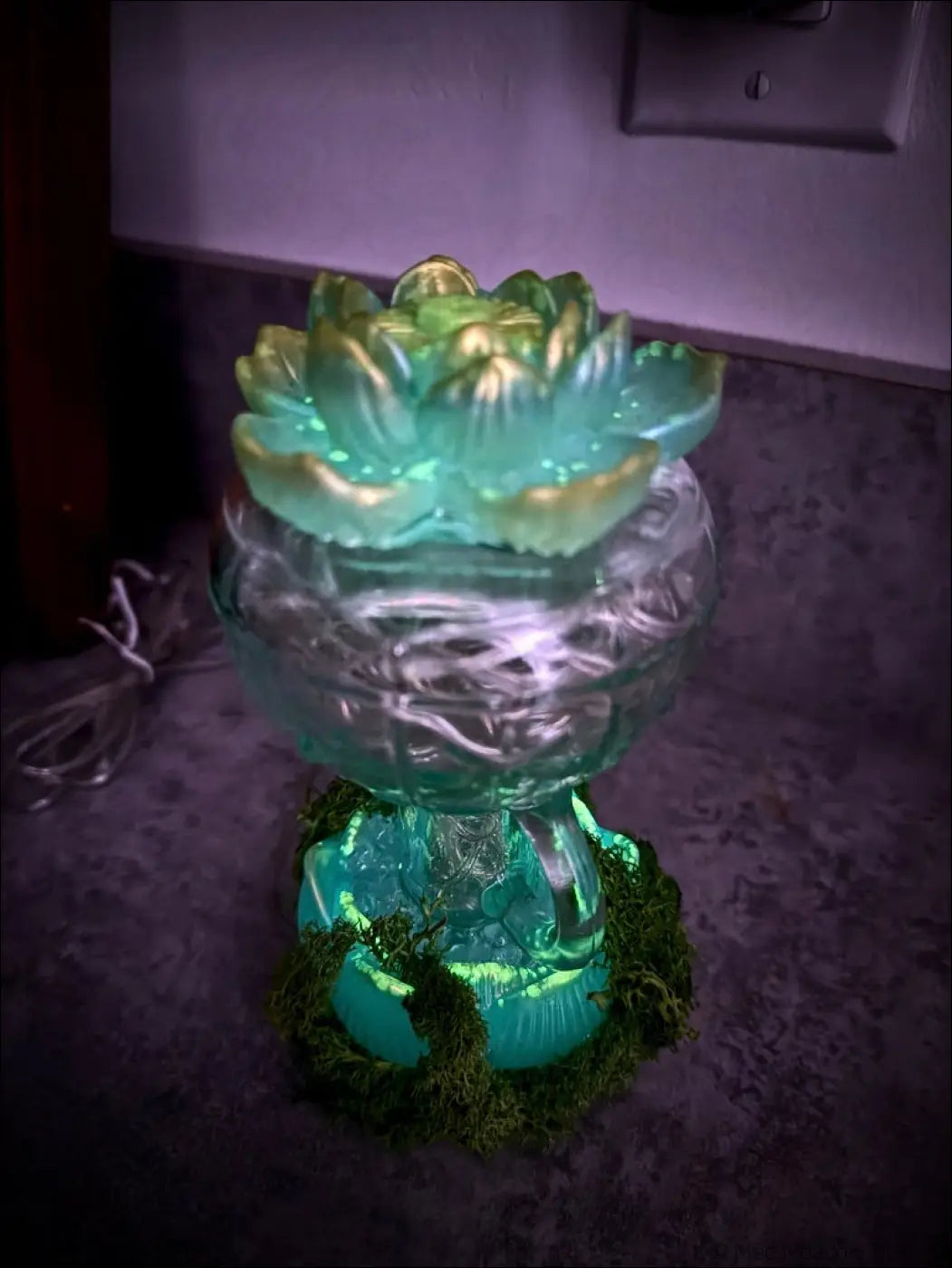 Mint green and gold lotus usb lamp with vintage glass base surrounded by green moss and white lights glowing bright