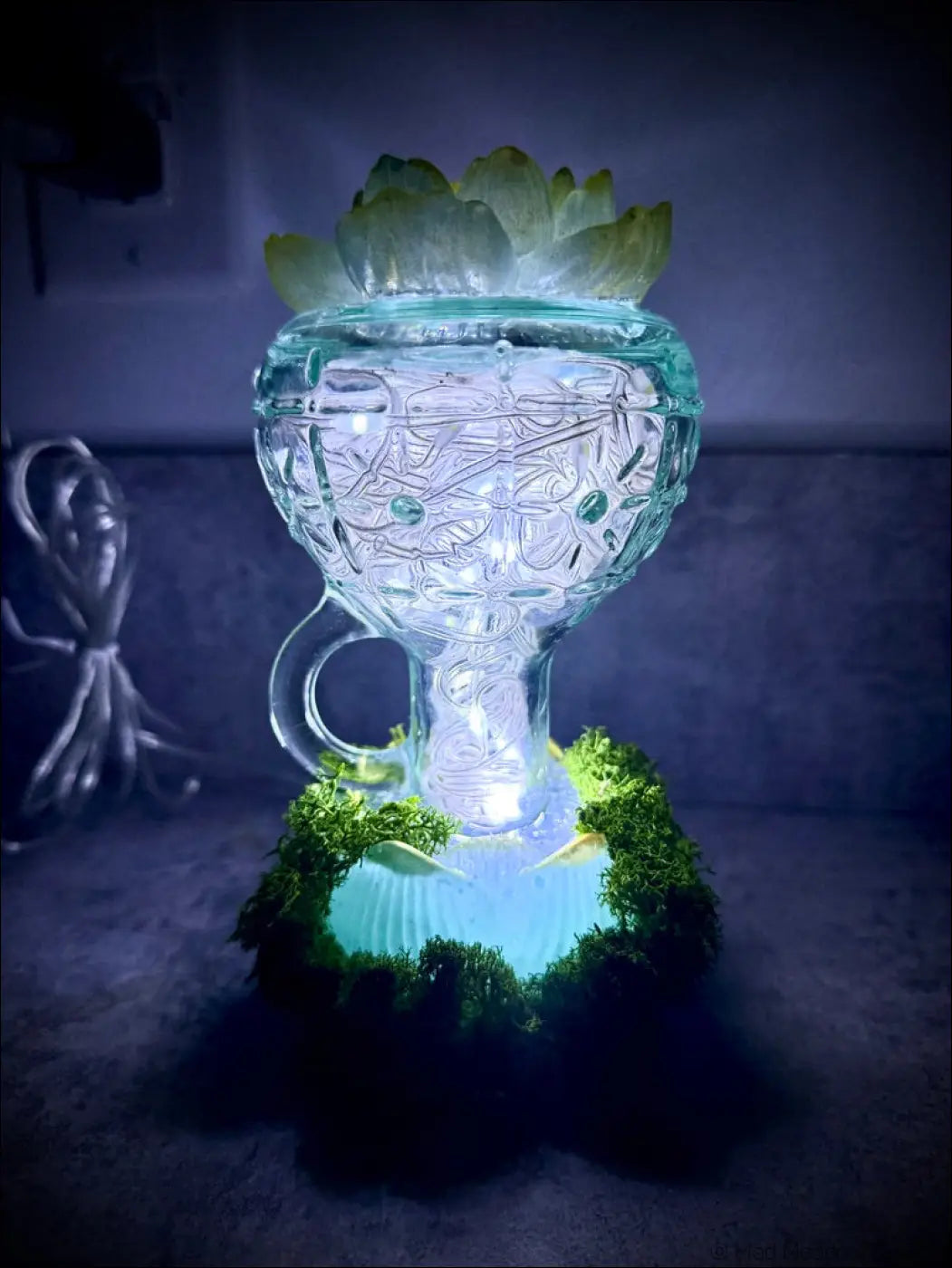 A mint green vintage glass lantern with gold lotus etching glowing blue light and a handle for easy carrying