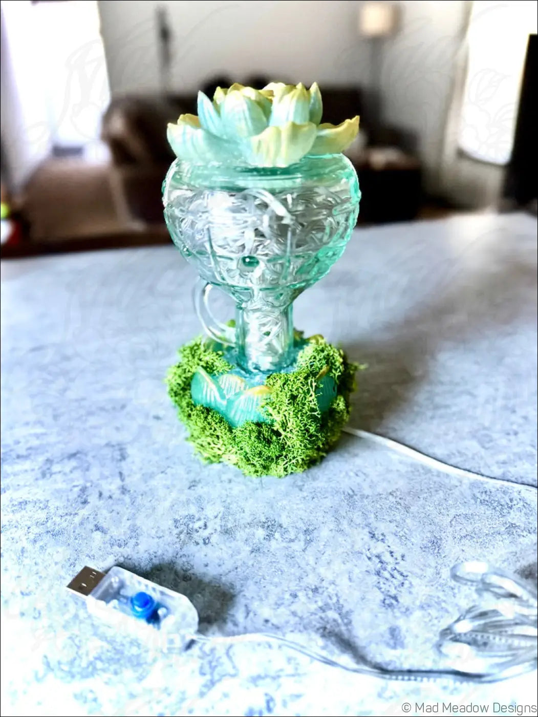 A mint green vintage glass lotus flower humidifier with etched patterns topped with a succulent and moss base