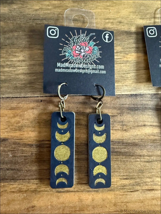 Dark blue rectangular wooden earrings with gold glitter moon phases design showcasing celestial magic style