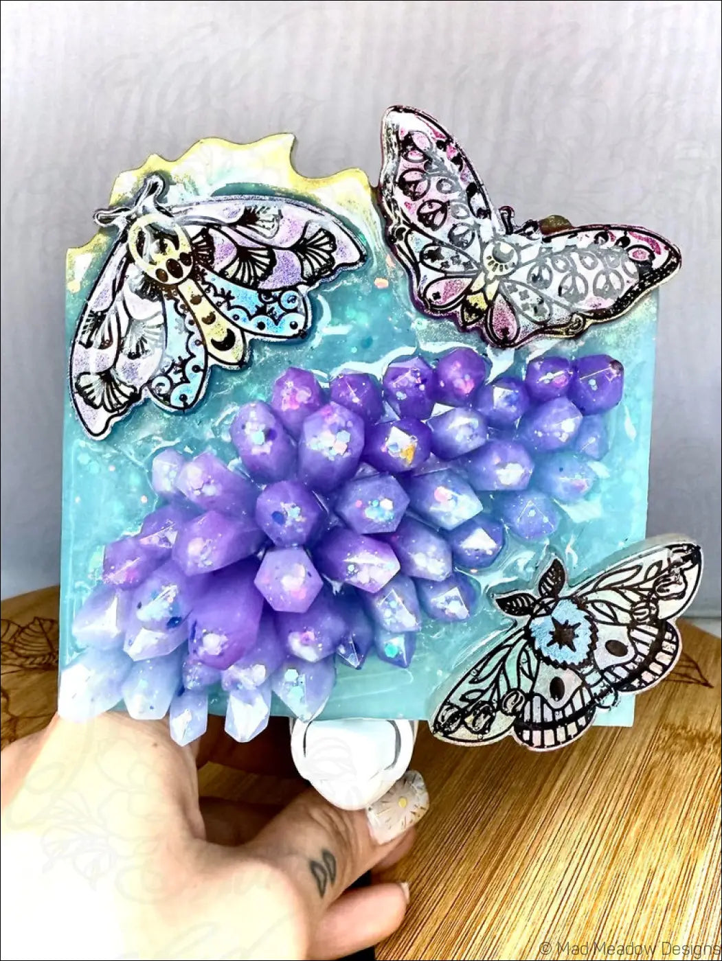 A handcrafted plug-in wall night light with delicate iridescent moths and a mesmerizing crystal cluster on soft aqua blue base