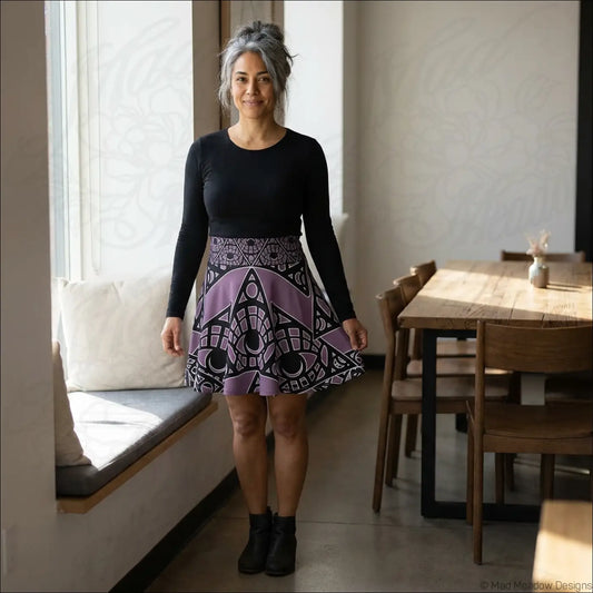 A woman wearing a black top with a purple and white mystic eye tribal skater skirt featuring a grape allover print