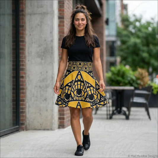 A vibrant yellow and black mystic eye tribal skater skirt with bold geometric eye-shaped motifs and printed care label