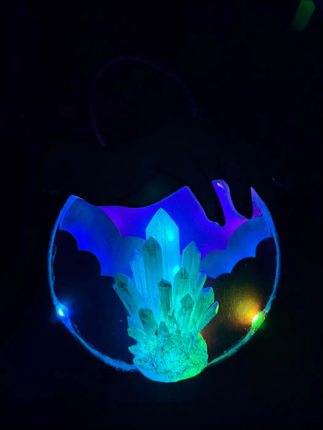 Mystical hand and hanging crystal ball with glowing blue and green crystal cluster in translucent bat frame