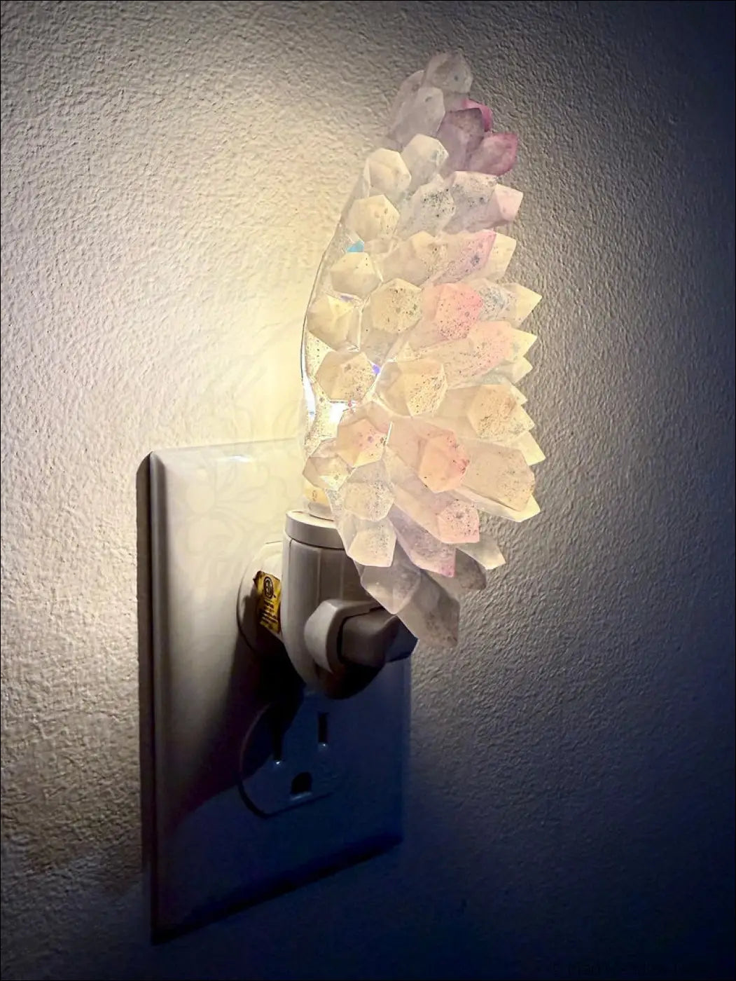 A pastel translucent white and purple crystal cluster resin wall night light with glowing faceted pieces on a plug-in base