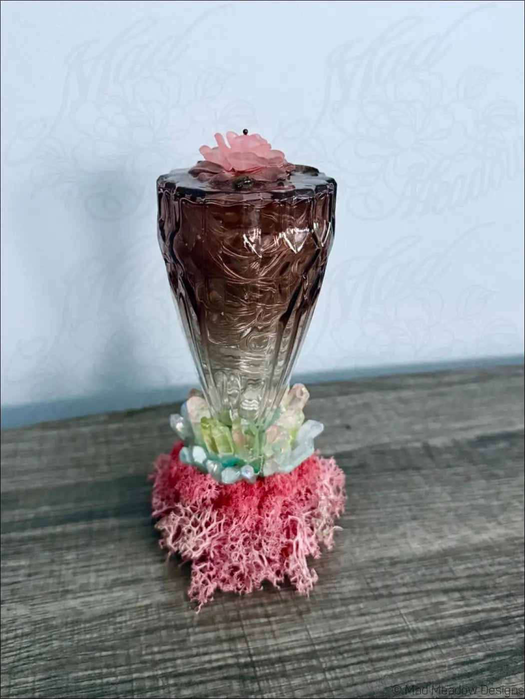 A translucent amber glass candle holder with etched patterns topped by a pink rose on a coral base with quartz crystal points usb light