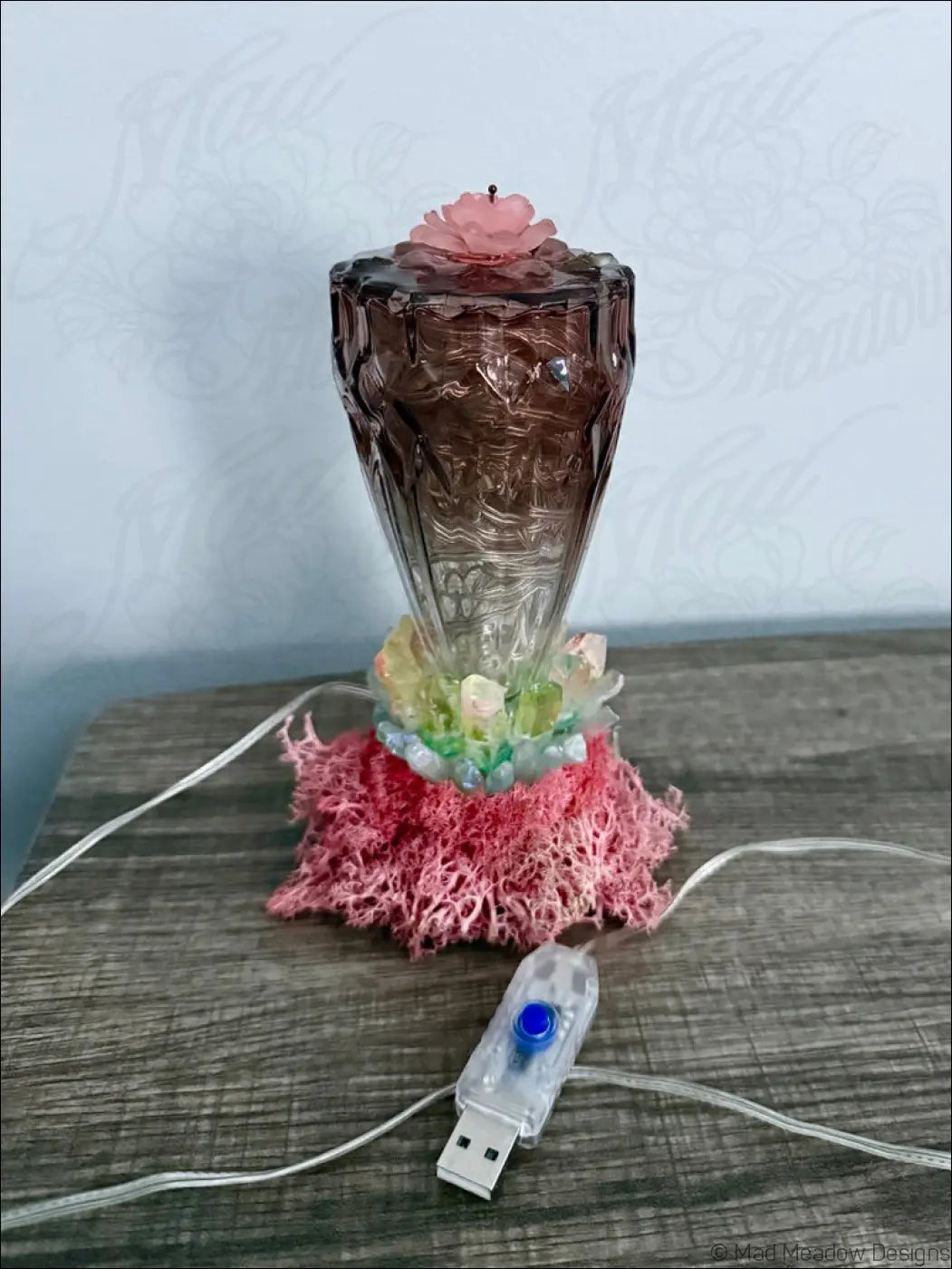A translucent amber usb light with etched patterns topped by a pink flower and quartz crystal points on a coral base