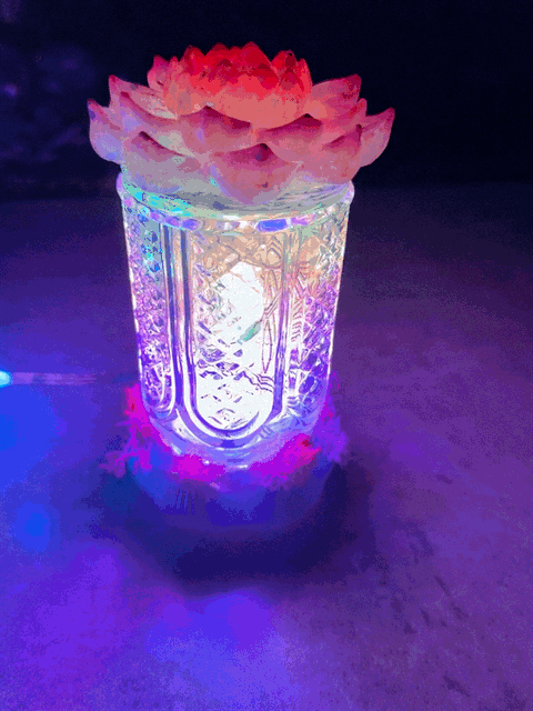 A glowing glass bud vase light with intricate etching and a pink lotus flower on top in pink fuchsia and purple resin
