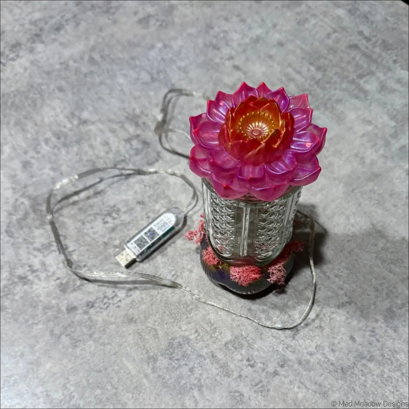 Pink lotus-shaped lamp with USB cable on a gray surface