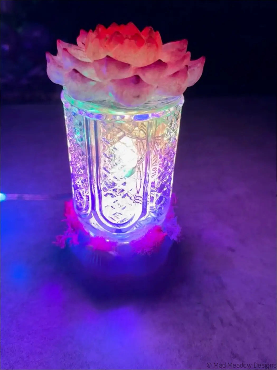 A translucent glass lantern with a glowing interior and pink lotus flower sculpture on top perfect as a bud vase