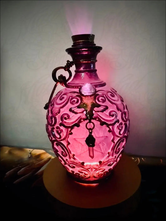 A glowing pink glass potion bottle light with intricate swirls dark metal handle and soft purple glow with crystal dangles