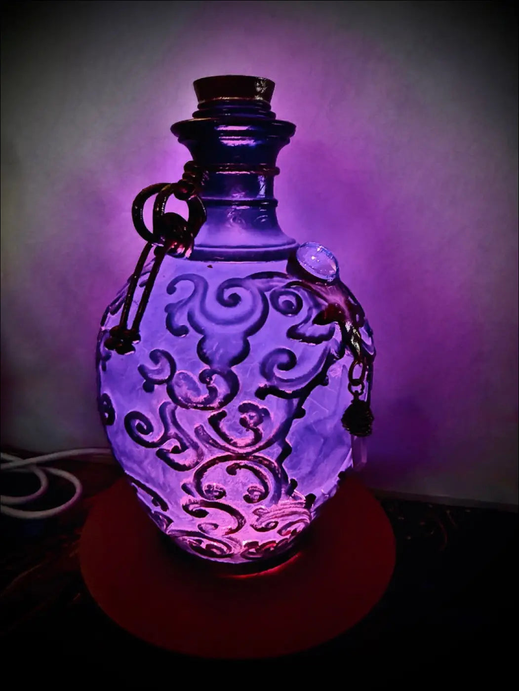 A translucent purple glass potion bottle light with black swirling etchings metallic keychain accents and a dark cork stopper
