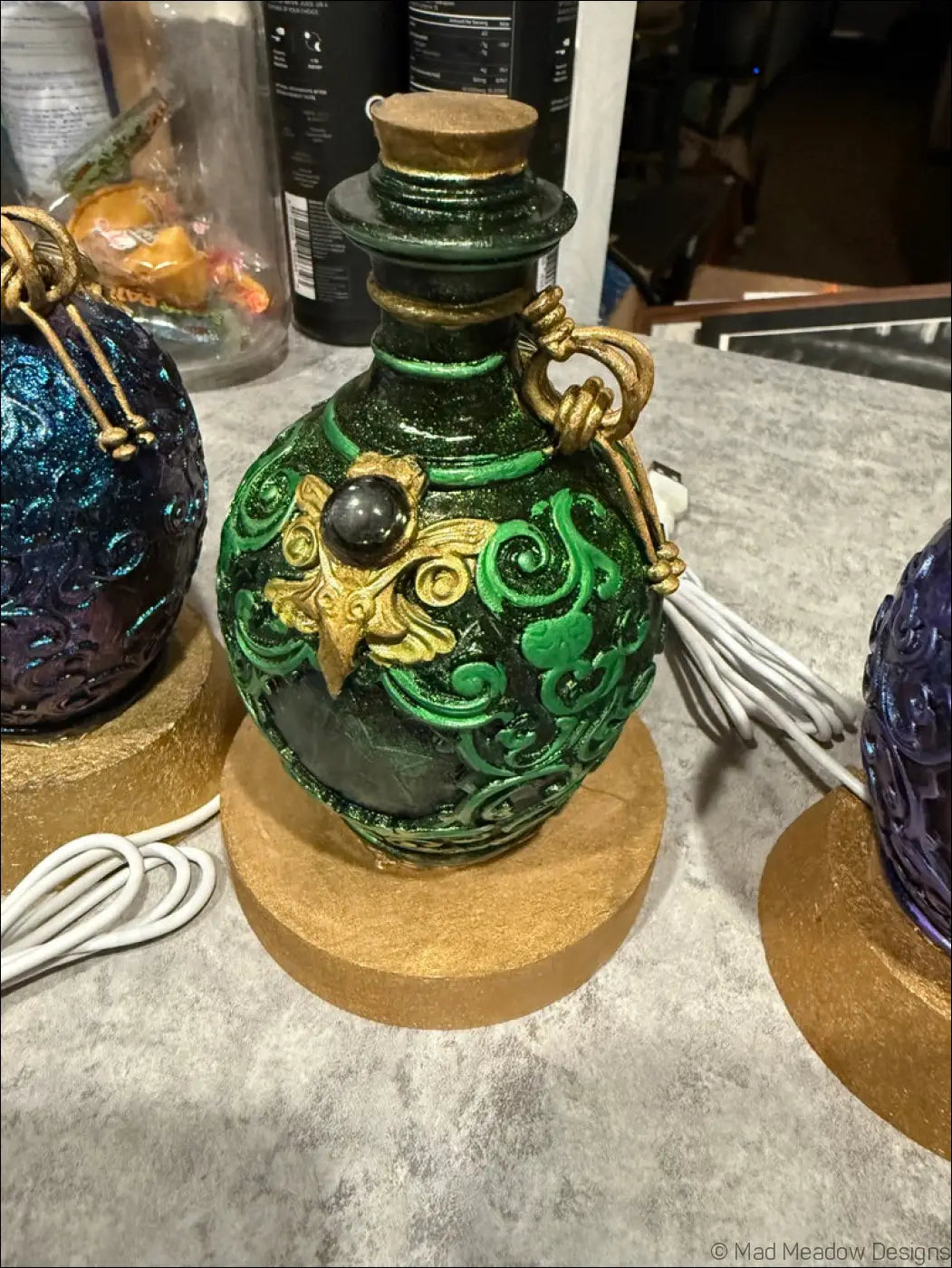 Green ornate potion bottle with gold accents cork stopper intricate patterns and black gem for white table light